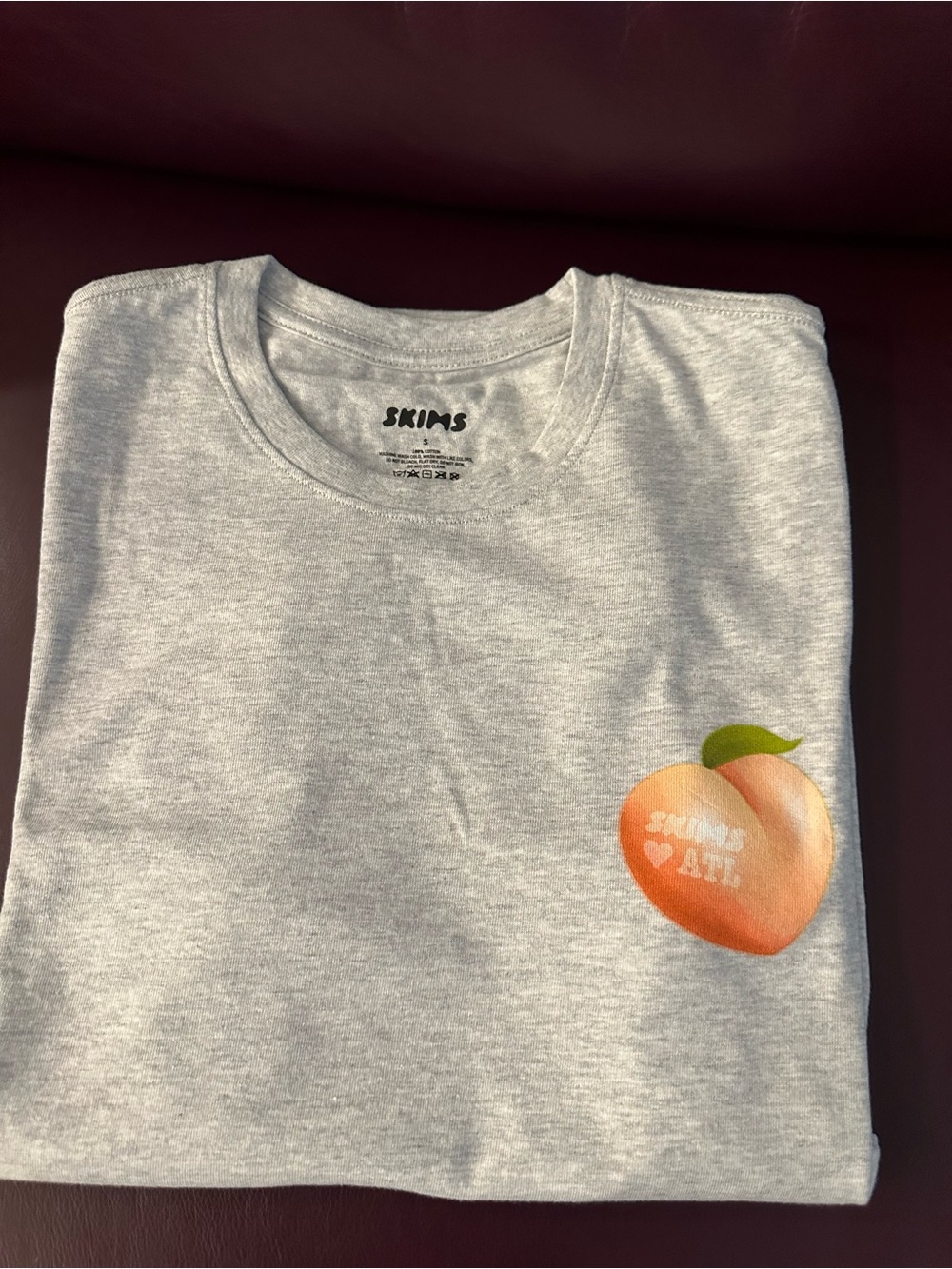 SKIMS ATL Anniversary Collection grey t-shirt featuring a front peach graphic